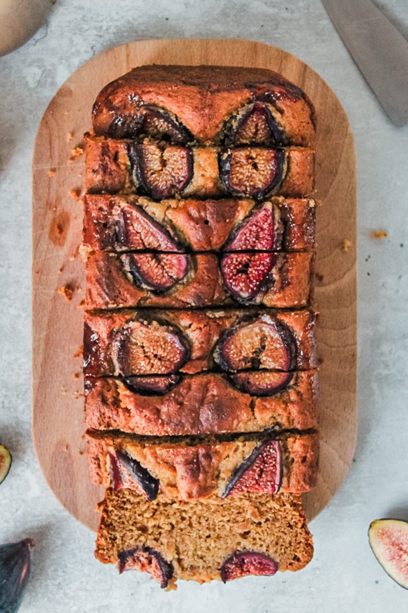 A sliced fig cake sits on a wooden board on a gray surface.