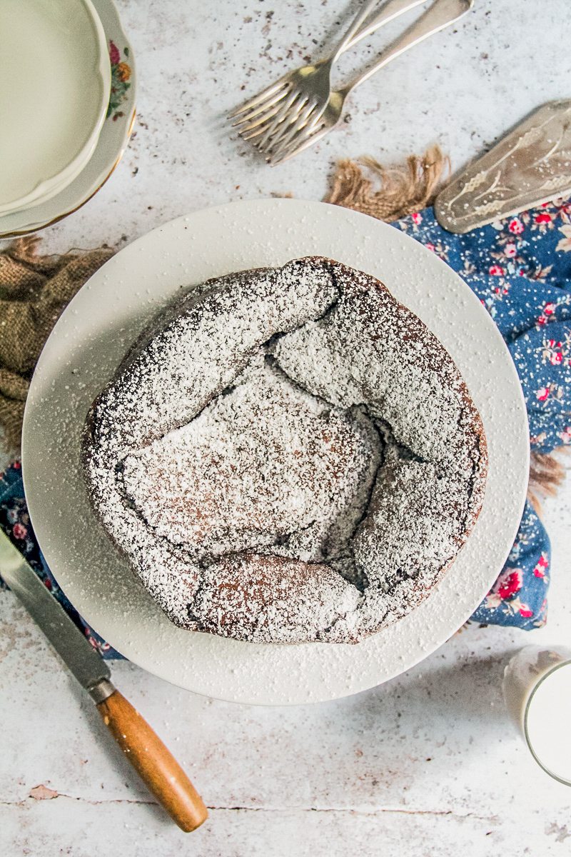 Flourless chocolate cake sits on a white ceramic plate topped with a sprinkle of powdered sugar above a light gray surface.