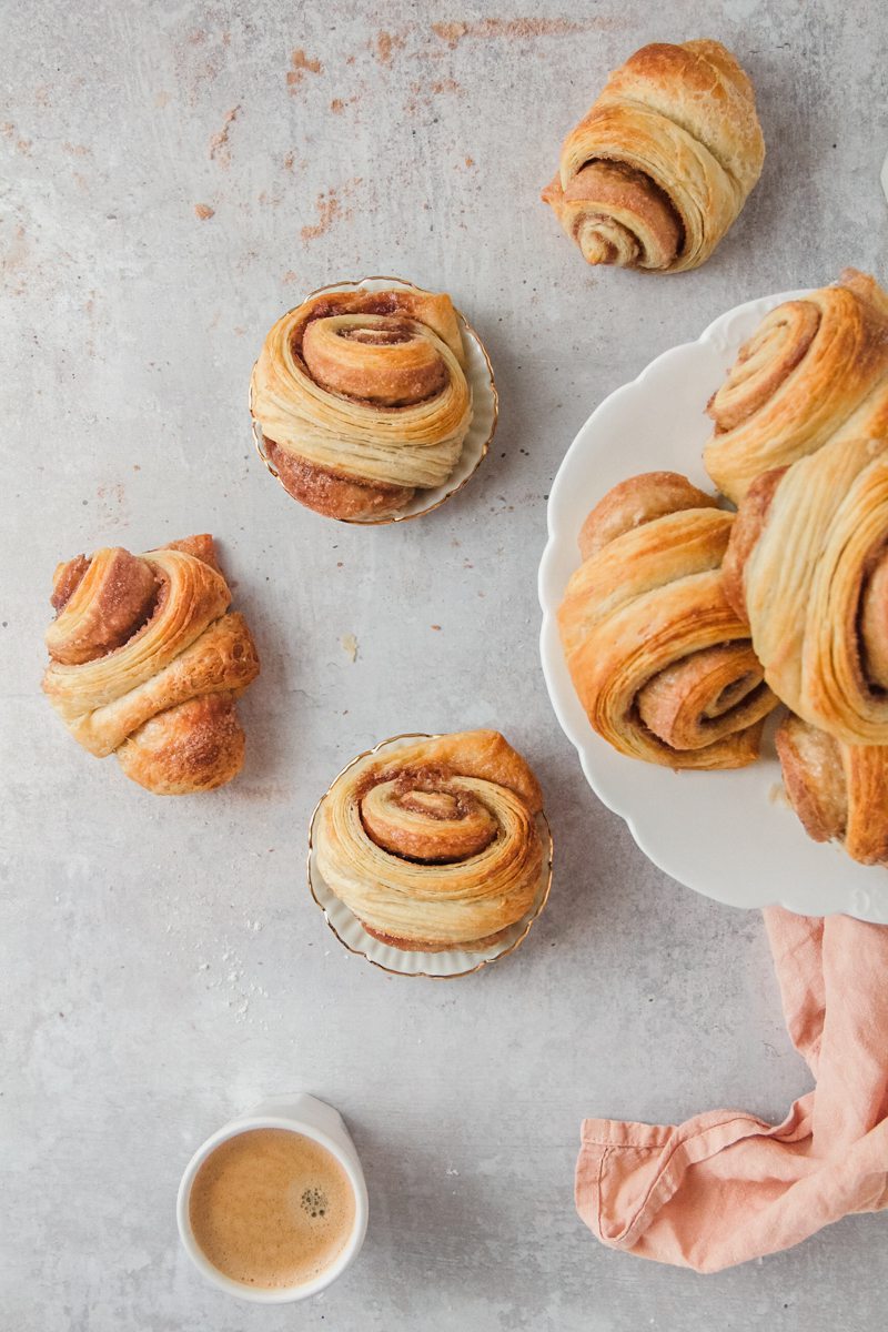 Franzbrotchen - German Cinnamon Rolls sit on individual small plates on a gray surface.