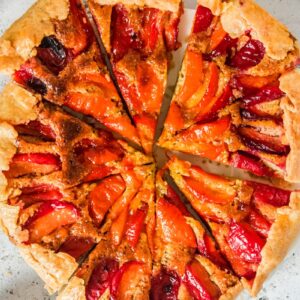 An apricot galette sits sliced on a white plate on a light gray surface.