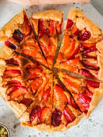 An apricot galette sits sliced on a white plate on a light gray surface.