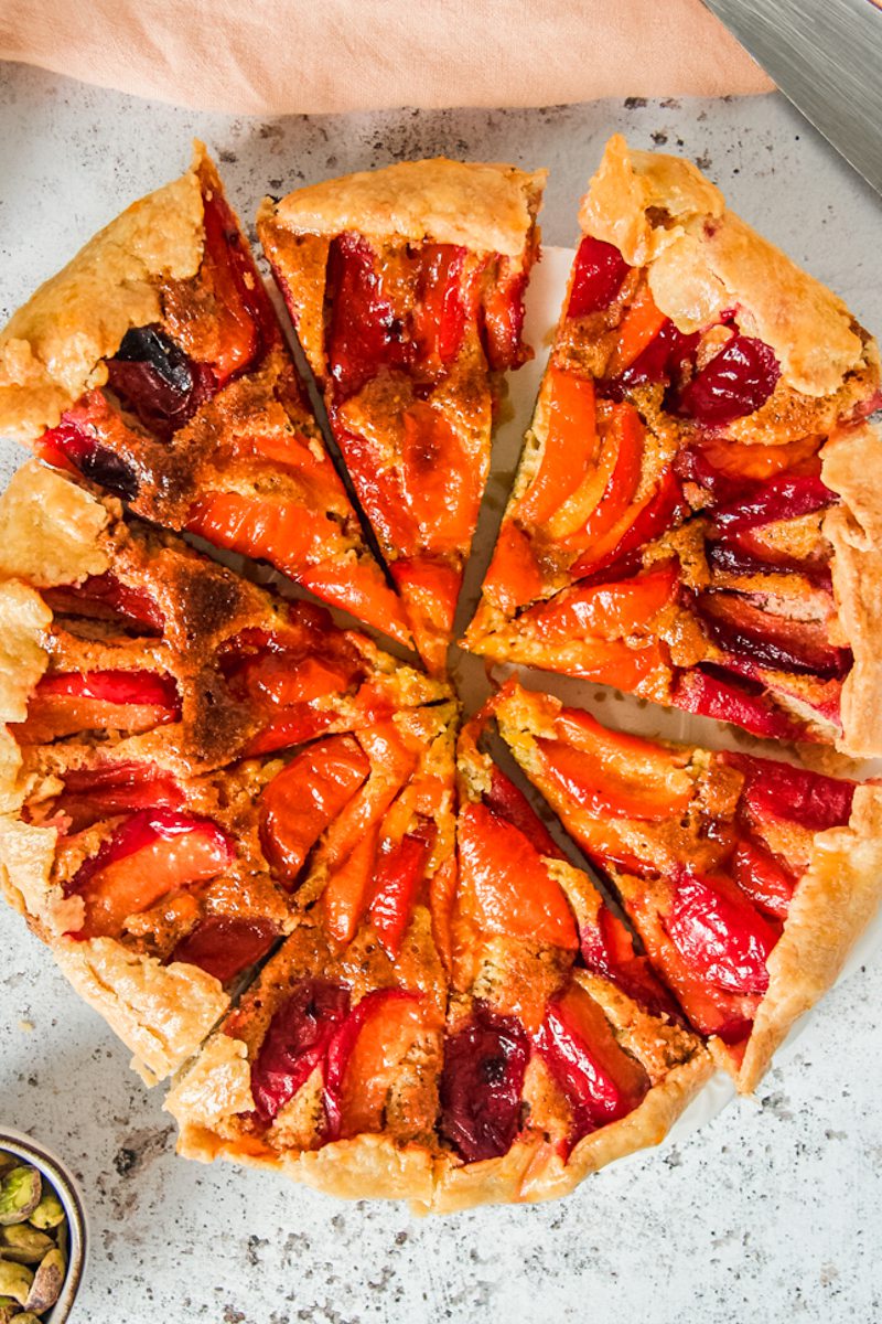 An apricot galette sits sliced on a white plate on a light gray surface.