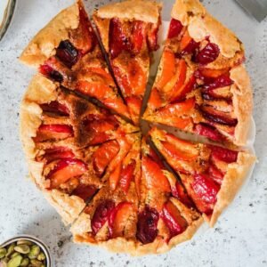 An apricot galette is sliced up and served on a light grey background.