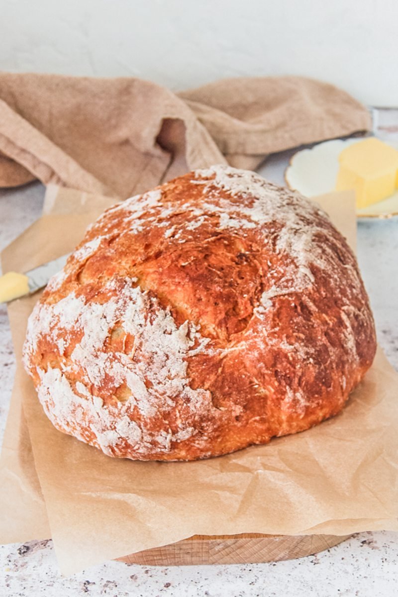 Potato bread sits on parchment paper on a wooden board on a gray surface with butter and a brown cloth in the background.