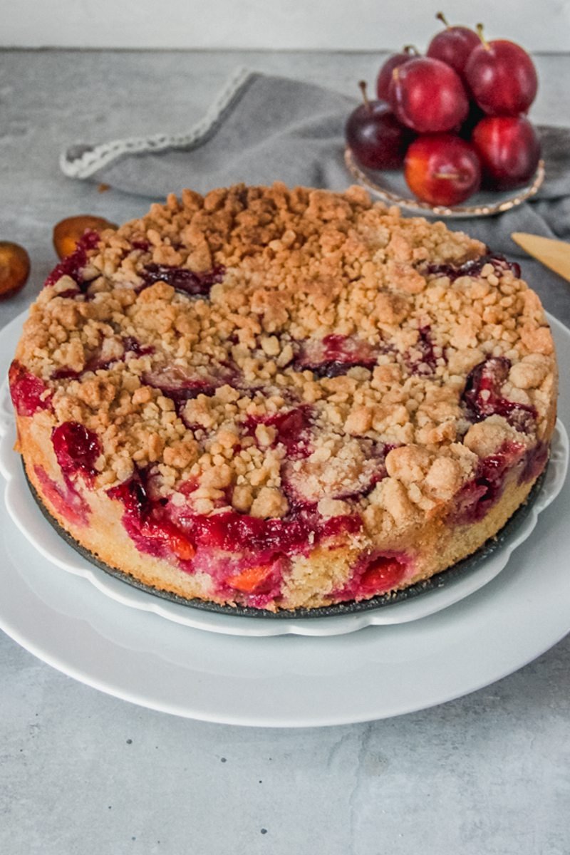 German plum cake sits on two white plates on a gray surface.