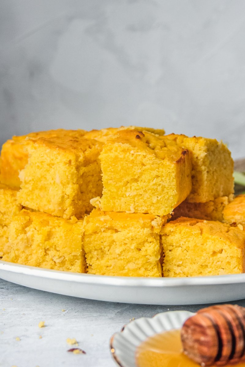 Squares of apple cornbread sit stacked on a white ceramic plate on a gray surface.