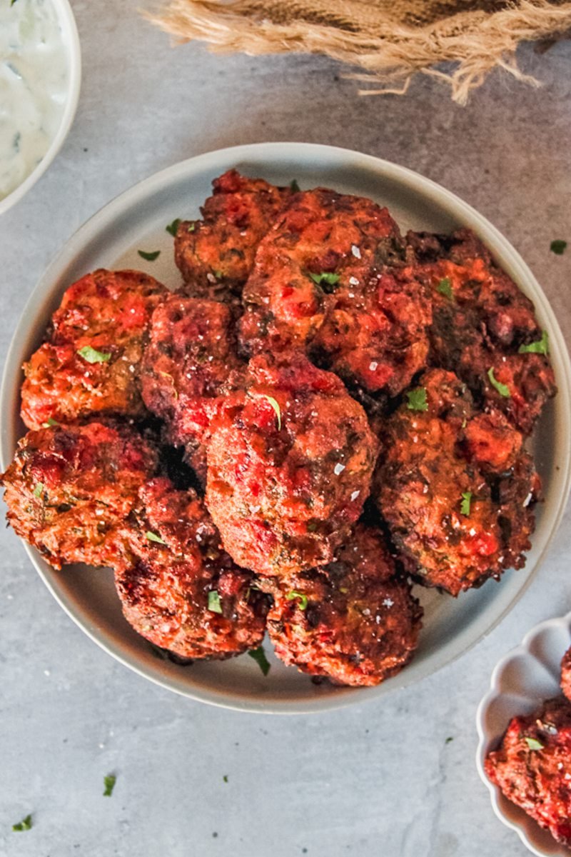 Greek tomato fritters are stacked on a stack of rimmed gray ceramic plates on a gray surface.