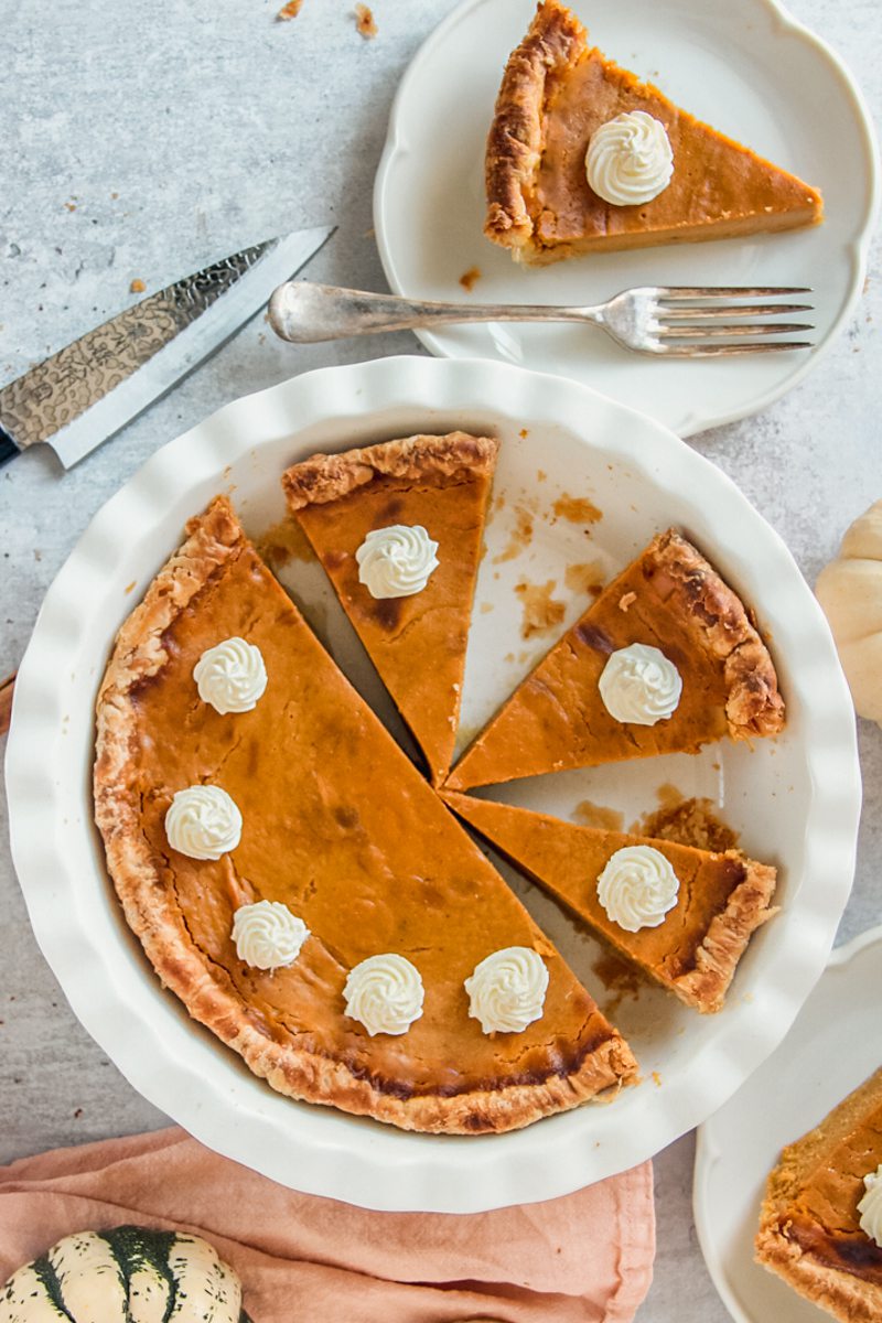 Pumpkin pie with slices cut into it sit in a white ceramic baking dish.