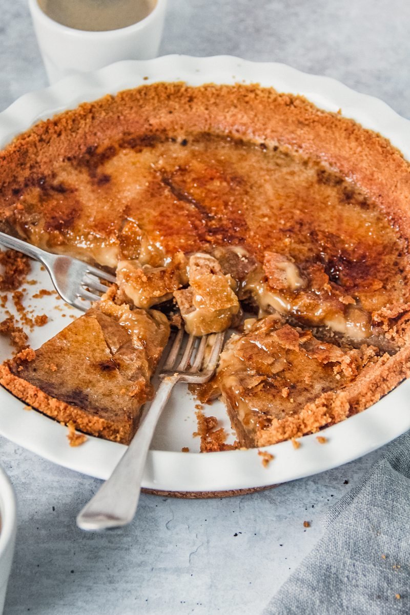 Pieces of coffee custard creme brulee pie has two forks sitting with servings scooped up in a white ceramic pie dish on a gray surface.