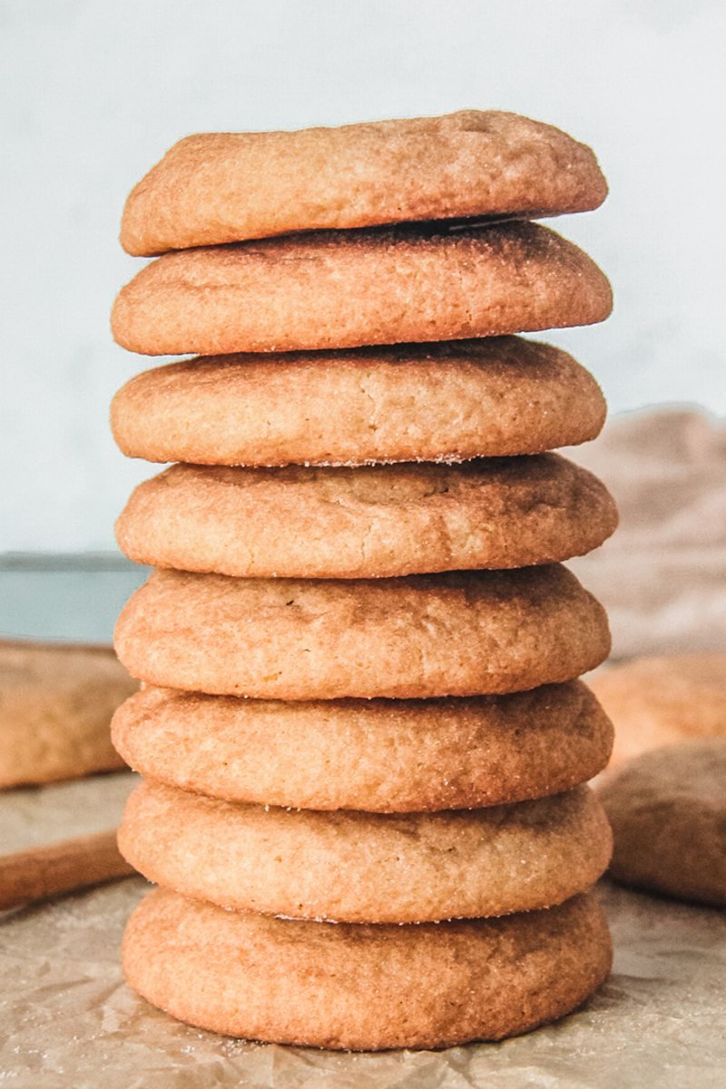 Snickerdoodle cookies sit stacked on each other on parchment paper.