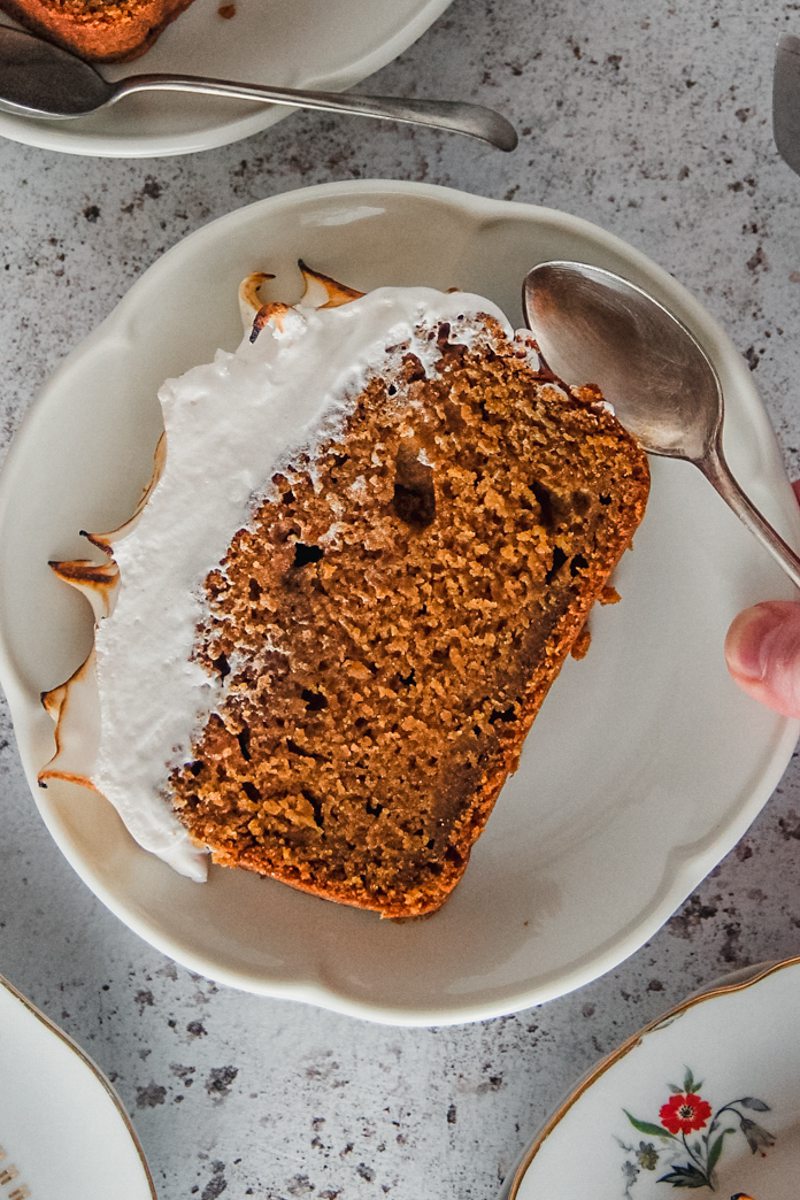 A slice of sweet potato loaf cake with a marshmallow topping sits on an individual serving plate on a light gray surface.