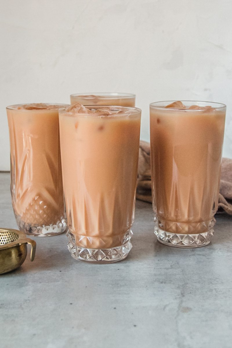 Servings of Thai ice tea sit in glasses on a gray surface.