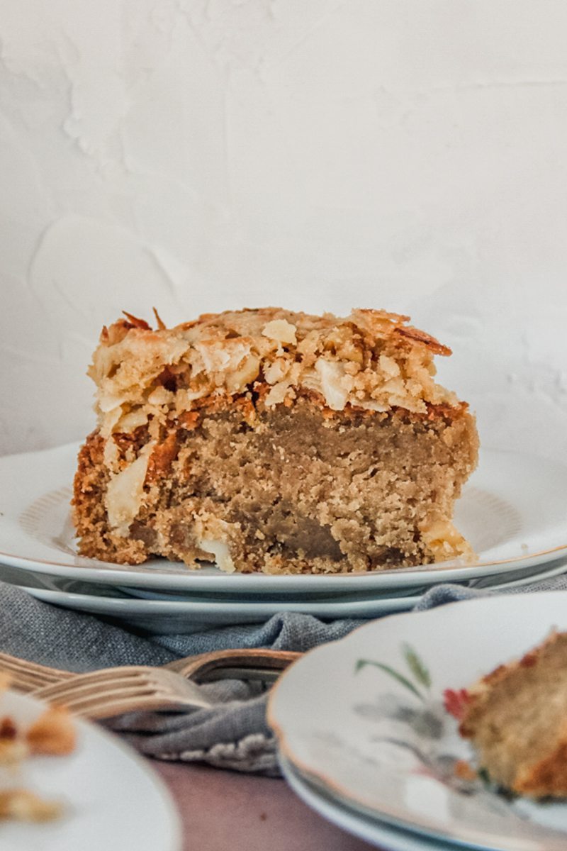 A slice of Irish oatmeal cake with a coconut topping sits on a two plates on a gray cloth.