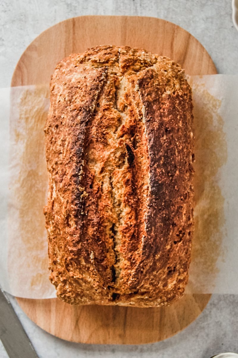 A loaf of Irish Brown bread sits on an oval wooden board on a gray surface.