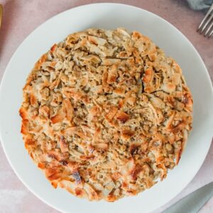 A whole Irish oatmeal cake sits on a white ceramic plate on a pink surface.