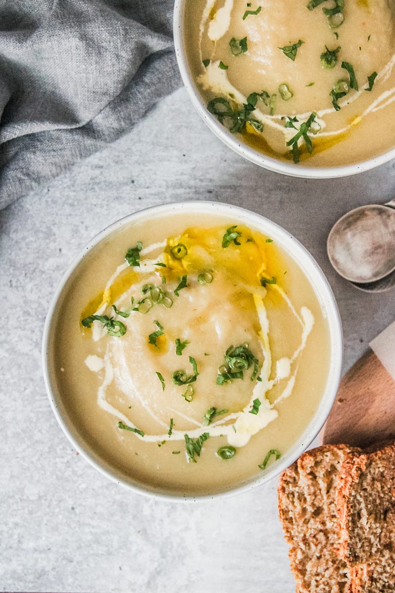 Individual servings of Irish potato soup sit in white round ceramic bowls beside a bowl of rice on a gray surface.