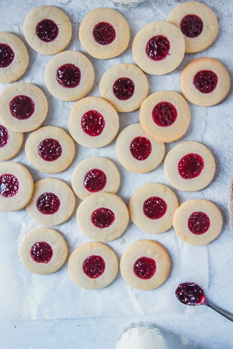 Swedish jam thumbprint cookies lay unevenly on a parchment paper lined gray surface.