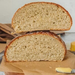 Kartoffelbrot or Potato bread sits cut in half on parchment paper on a wooden board on a gray surface with butter in the background.