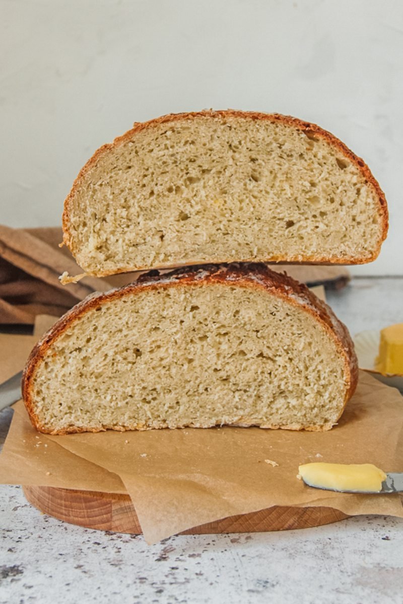 Kartoffelbrot or Potato bread sits cut in half on parchment paper on a wooden board on a gray surface with butter in the background.