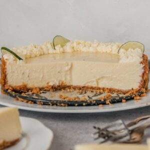 A halved key lime cheesecake with it's creamy filling sits on a white ceramic plate on a gray surface with a few slices of cake beside.