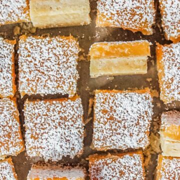 Lemon shortbread bars sit on a parchment paper lined surface with a few sitting on their side showing the shortbread base and lemon curd topping visible.