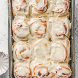 Brioche style fluffy lemon rolls sit on a light gray surface in a rectangle metal baking tin.