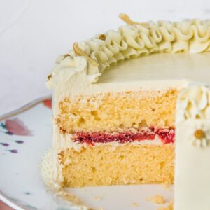 The interior of a lemon strawberry cake with a roasted strawberry center frosted with a chamomile Swiss buttercream frosting sits on a cake strand above a light gray surface.