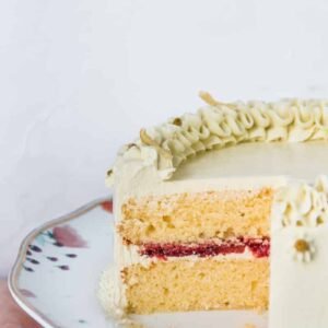 A Lemon Strawberry layer Cake is served on a plate with a slice cut out to show off it's bright interior, roasted strawberry center and chamomile swiss meringue buttercream.