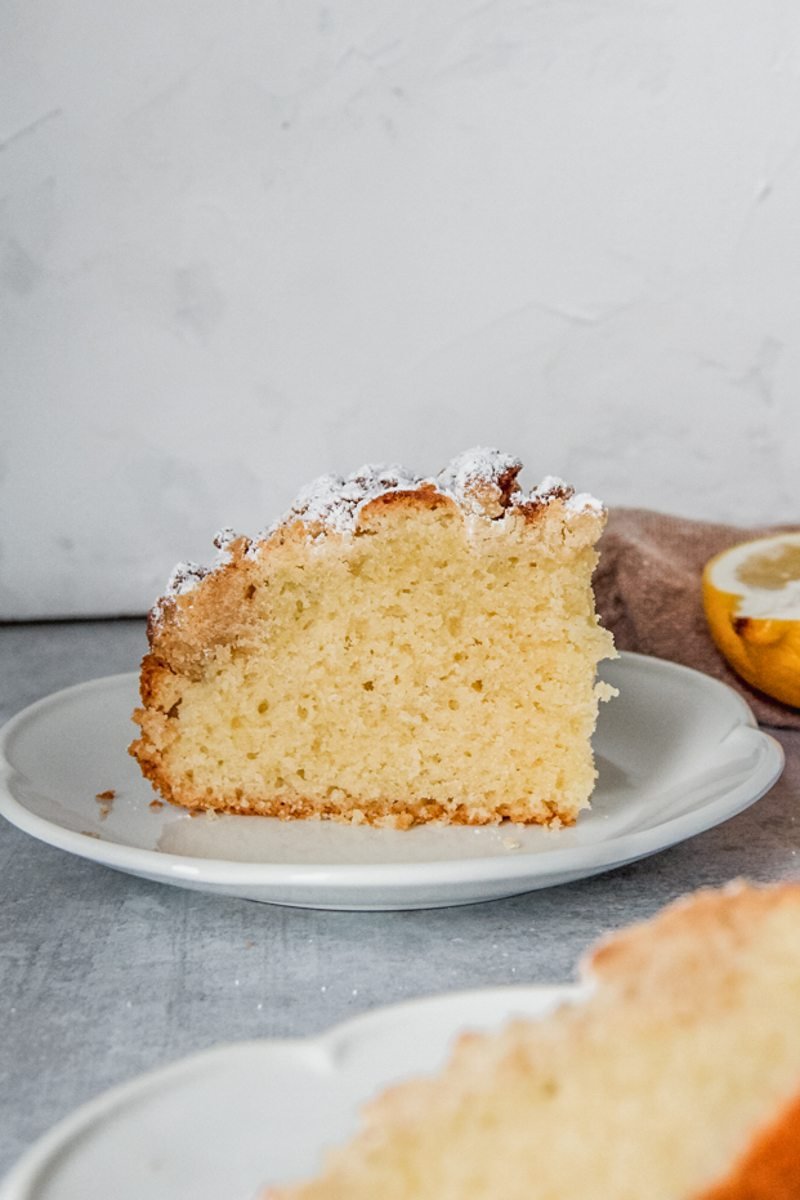 A piece of dairy free olive oil cake sits on a white ceramic plate.