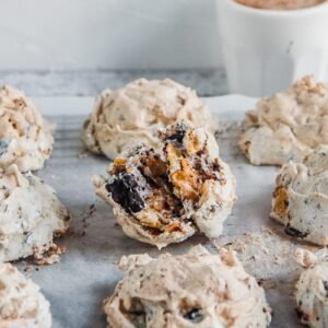 A Marens Kornflexkokur or Iceland chocolate cornflake cookies sit on parchment paper on a cooling rack with a small cup of coffee behind on a light gray surface.