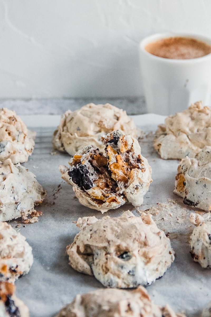 A Marens Kornflexkokur or Iceland chocolate cornflake cookies sit on parchment paper on a cooling rack with a small cup of coffee behind on a light gray surface.