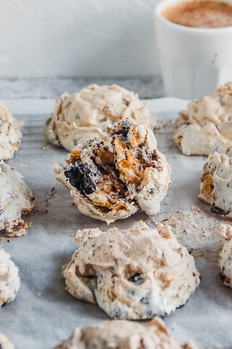 A close up of Marens Kornflexkokur or Iceland chocolate cornflake cookie sitting on parchment paper on a cooling rack with a small cup of coffee behind on a light gray surface.