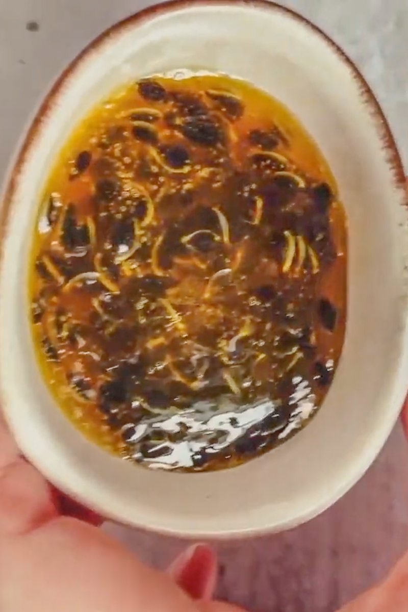 Passionfruit syrup sits in a small bowl held above a gray surface.