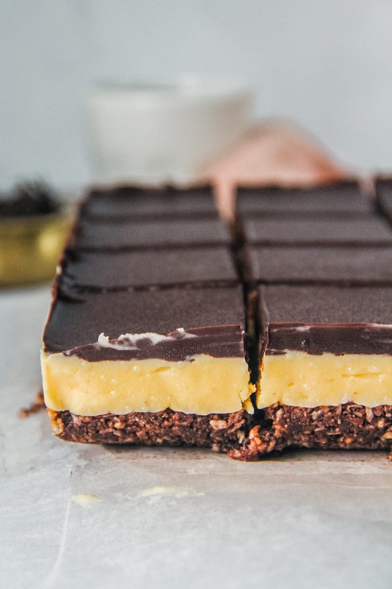 A side shot of sliced Nanaimo bars sitting on a lined gray surface.