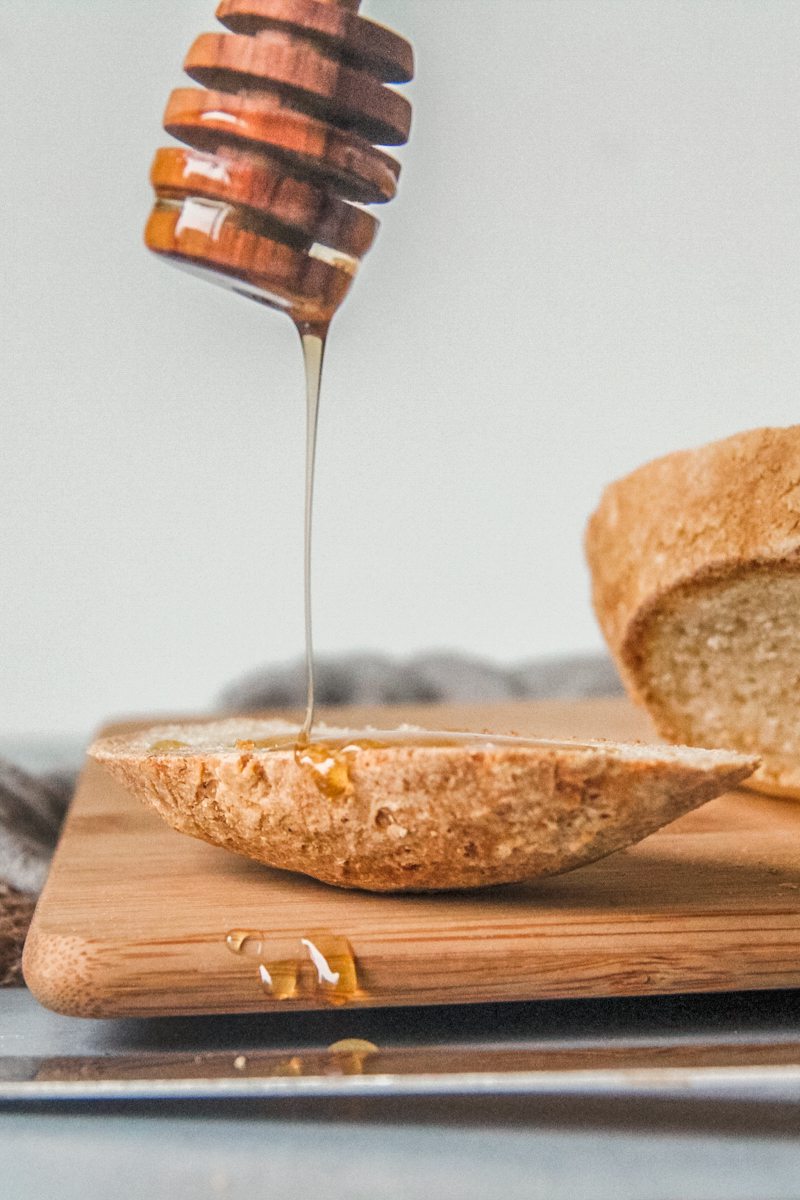 Honey is drizzled onto an end piece of bread sitting on a wooden board on a blue surface.