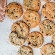 NY Times Chocolate Chip cookies lay on a light gray surface with one cookie split in half and resting on others.