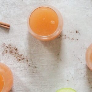 Glasses of homemade apple cider sit on a gray surface.