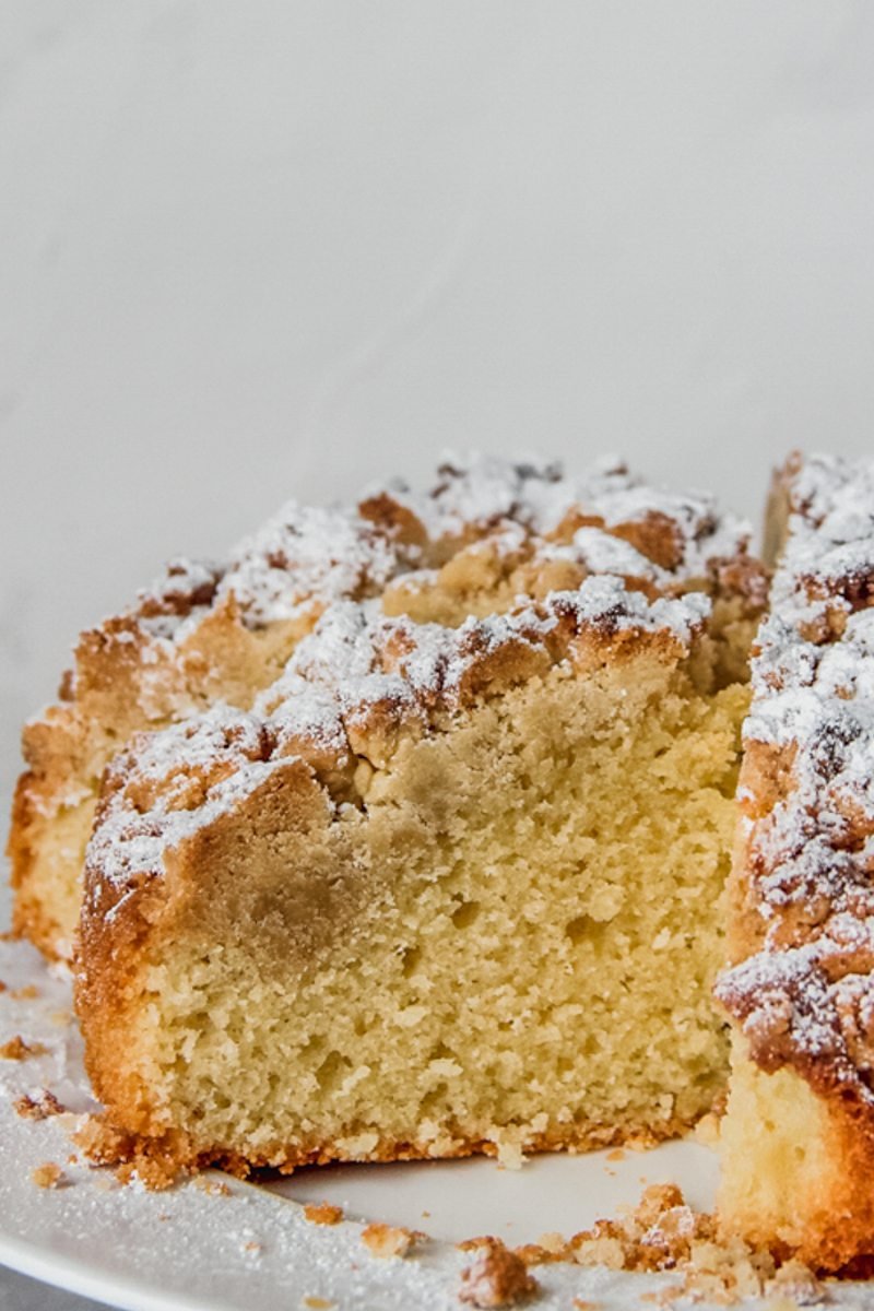 A close up image of a dairy free olive oil cake topped with an olive oil crumble served up on a white plate.