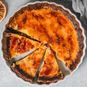 Orange custard pie sits in a white ceramic baking dish with a few slices cut out.