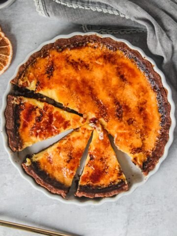 Orange custard pie sits in a white ceramic baking dish with a few slices cut out.