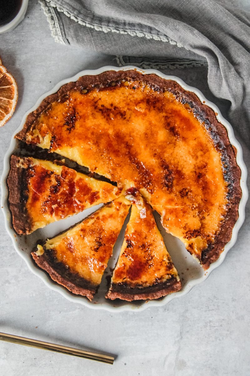 Orange custard pie sits in a white ceramic baking dish with a few slices cut out.