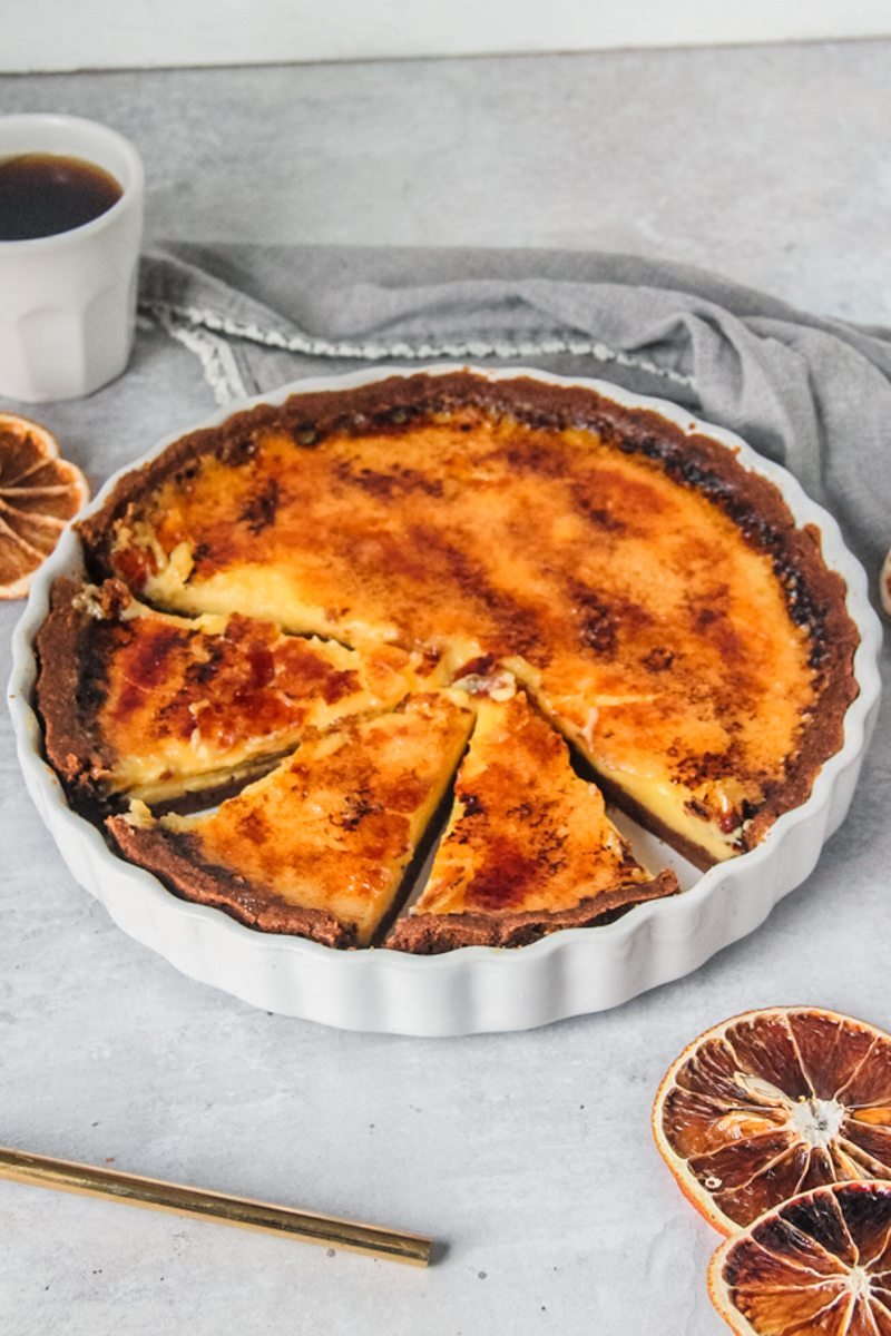 Orange custard pie sits in a white ceramic tart dish with a few slices cut out on a gray surface.