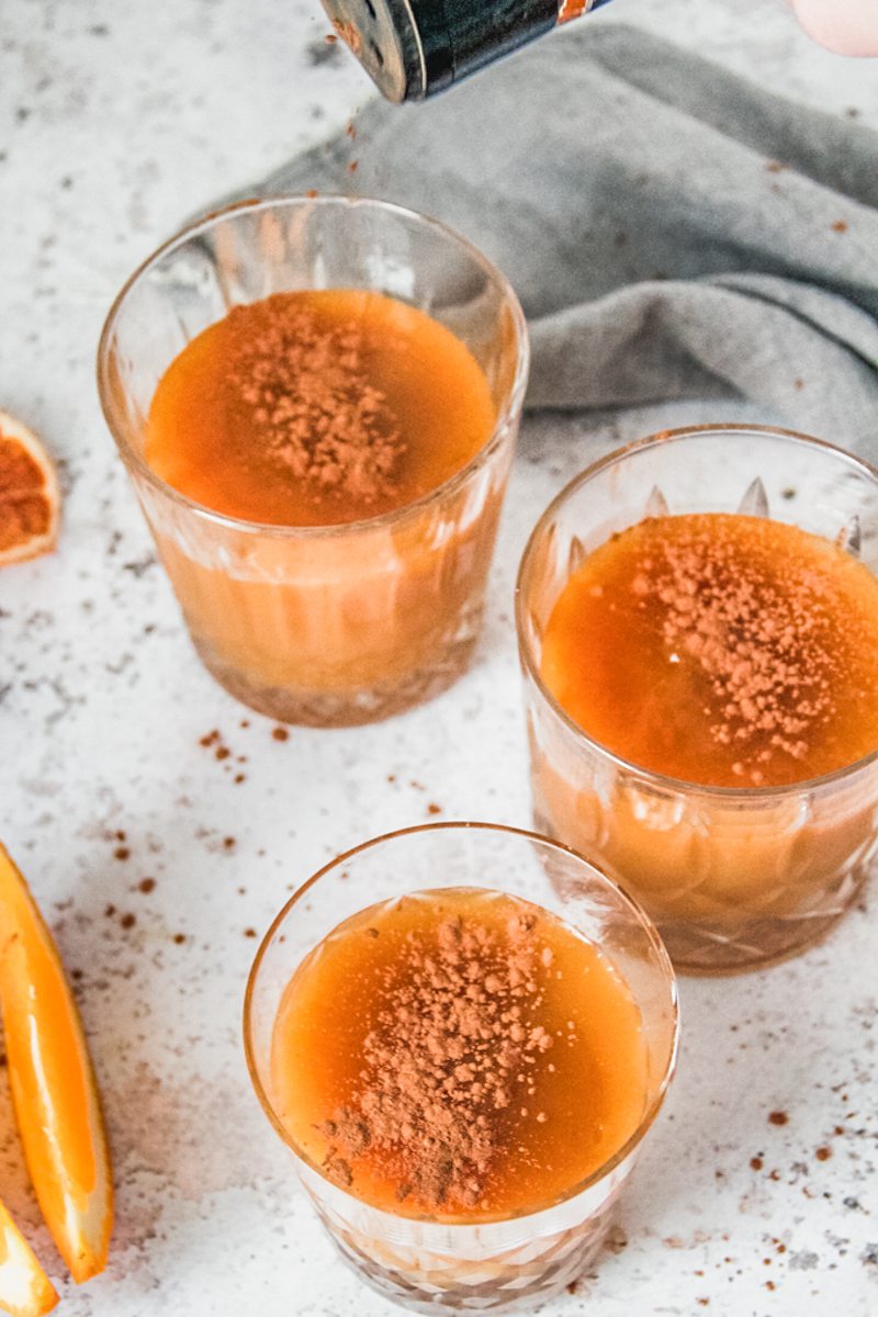 Individual servings of Costa Rican Orange Pudding topped with ground cinnamon sit on a light gray surface.