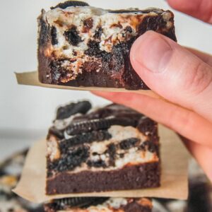 A piece of fudgy oreo cheesecake brownie is held with a bite taken out.