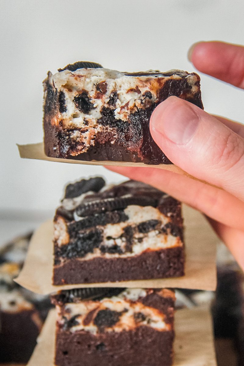 A piece of fudgy oreo cheesecake brownie is held with a bite taken out.