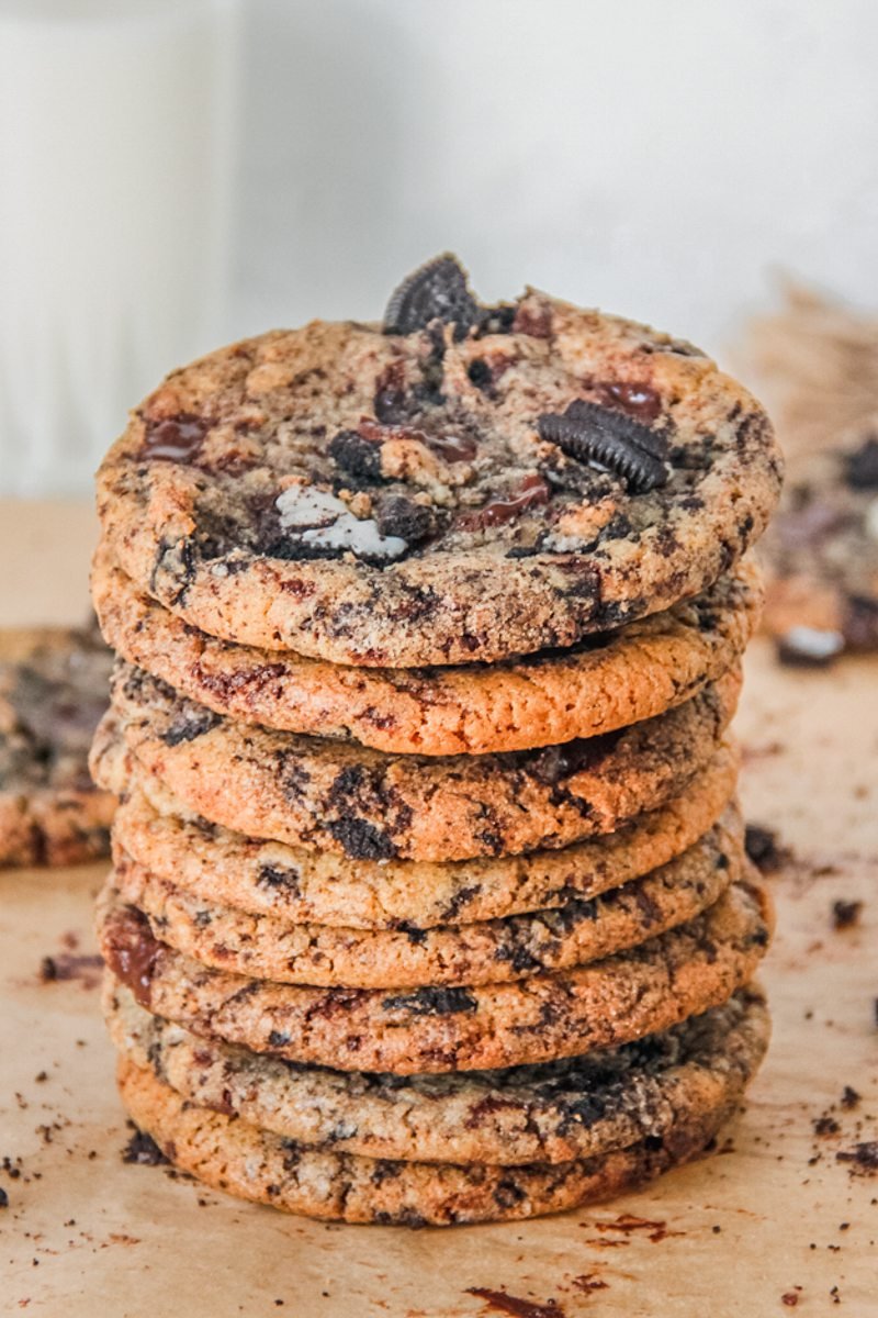 A stack of Oreo chocolate cookies sit on parchment paper with a glass of milk in the background.