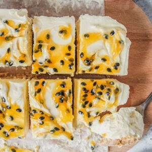 Slices of cheesecake sit on a wooden board with one spooned into on a light gray surface.