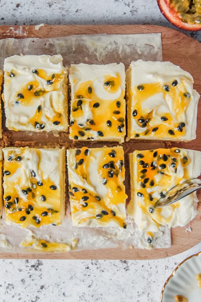 Slices of cheesecake sit on a wooden board with one piece being spooned into on a light gray surface.