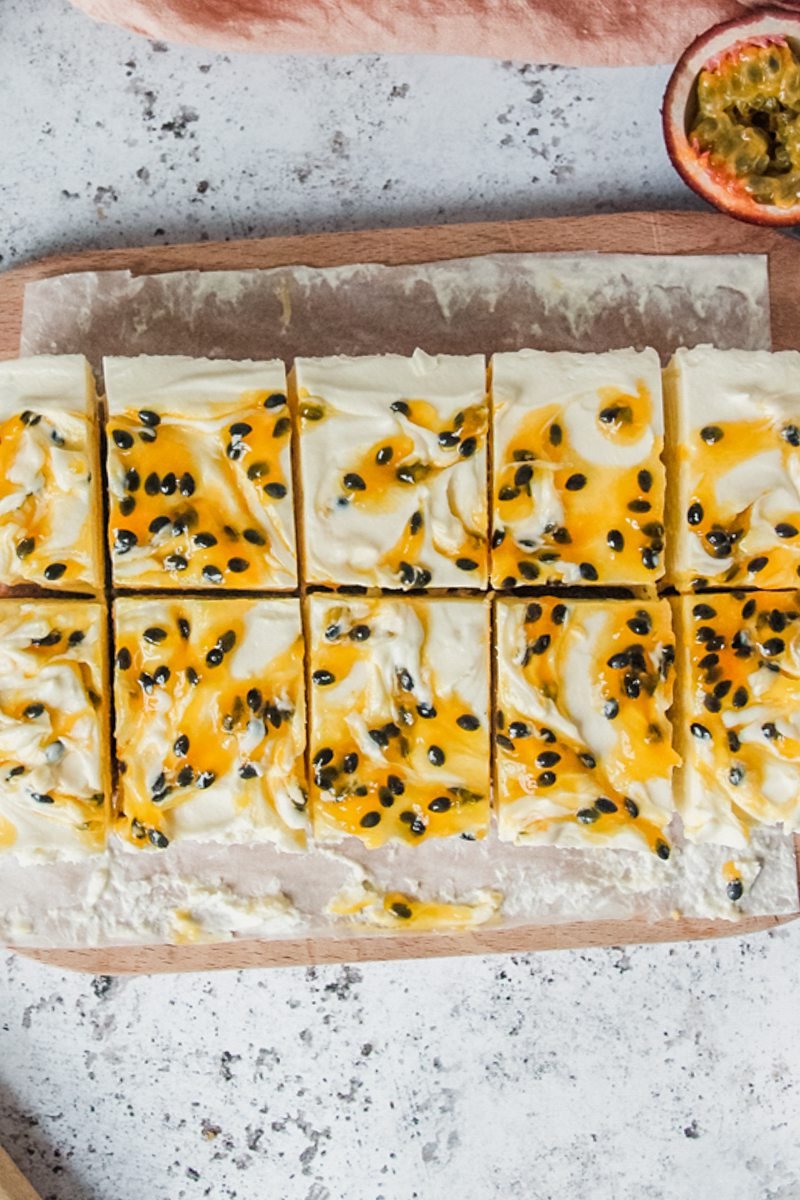 Slices of swirled passionfruit cheesecake sit on a wooden board on a light gray surface.