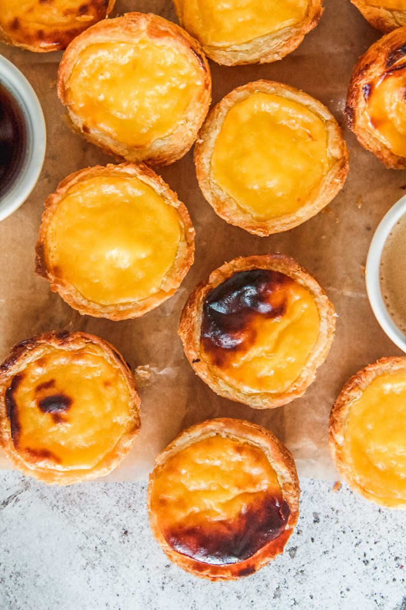 Pasteis de Natas sit on parchment paper on a light gray surface.